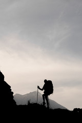 Silhouette slim girl standing on the rock with hiking backpack and walking sticks
