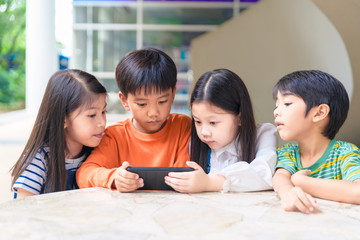 group of asian kids play game on smartphone together, smiling small brother and sister have fun hold using cellphone, watch funny cartoon. Children and technology concept