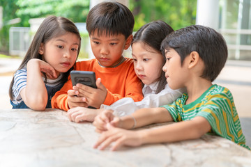 group of asian kids play game on smartphone together, smiling small brother and sister have fun hold using cellphone, watch funny cartoon. Children and technology concept