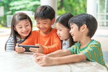 group of asian kids play game on smartphone together, smiling small brother and sister have fun hold using cellphone, watch funny cartoon. Children and technology concept © Songkhla Studio