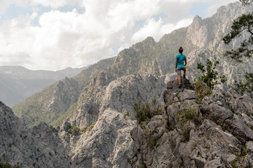 Rear view girl in the blue shirt standing on the rock on the beautiful landscape