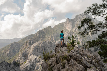 Naklejka premium Rear view sporty girl standing on the rock on the beautiful landscape