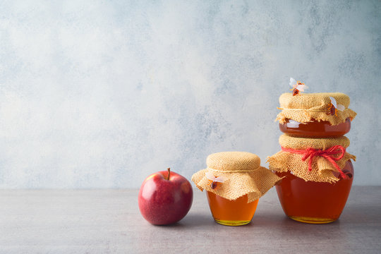 Honey jars and apple over grey background