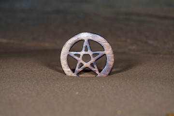 Wooden encircled Pentagram symbol on the beach at sunrise in front of the lake. Concept of Five...