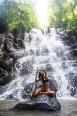 Fototapeta na wymiar Woman practices yoga near waterfall in Bali, Indonesia