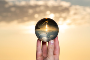 Woman's hand holding high grade Clear Quartz Sphere at the sunrise in front of the lake.
