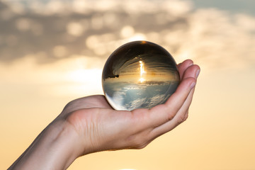 Woman's hand holding high grade Clear Quartz Sphere at the sunrise in front of the lake.