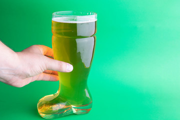 A hand holding a beer boot glass in green background