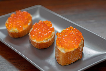 Three slices of bread with butter and salmon caviar in a grey rectangular plate..