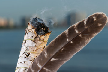 Smudging Ritual using burning thick leafy bundle of White Sage Grade A barred Turkey Smudging Feather on the beach at sunrise in front of the lake.