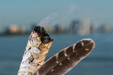 Smudging Ritual using burning thick leafy bundle of White Sage Grade A barred Turkey Smudging Feather on the beach at sunrise in front of the lake.