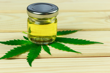 bottle of hemp oil on hemp leaves, bright wooden background