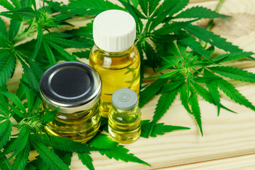glass bottles, different shapes, with hemp oil among hemp leaves, light wooden background