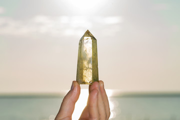 Woman holding Polished CITRINE point in her hand at sunrise in front of the lake.