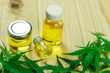 glass bottles, different shapes, with hemp oil among hemp leaves, light wooden background