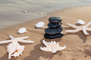 Fototapeta na wymiar Spa composition - stacked Basalt Stones, Seashells and Sea Stars on the beach at sunrise in front of the ocean. Wellness, Balance and Relax concept.