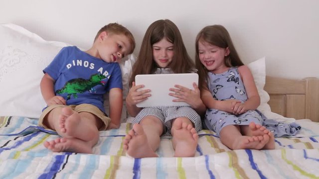 happy children, brother and sisters, best friends are sitting on the bed watching cartoons on the tablet. play computer games, use gadgets