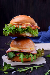 Two sandwiches with arugula salad, brisket and cheese against dark background
