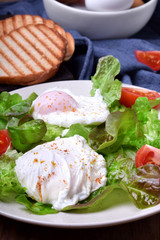 Poached eggs, tomatoes and green salad on a white plate