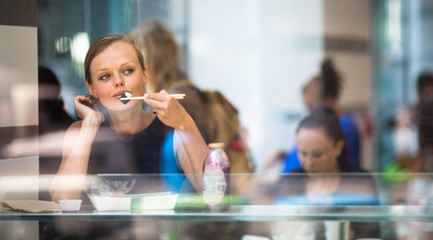 Pretty, young woman eating sushi in a restaurant, having her lunch break, enjoying the food,...