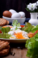 Poached egg with liquid yolk and green salad on a white plate