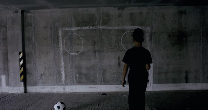 Teenager kid boy soccer player using a spray paint to draw goals and targets on a wall in empty abandoned covered parking. 4K UHD 60 FPS RAW graded footage