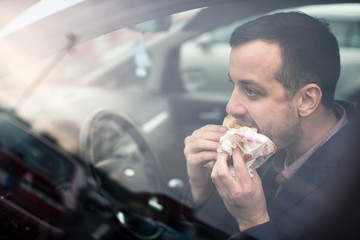Handsome young man eating a hurried lunch in his car (color toned image; shallow DOF)