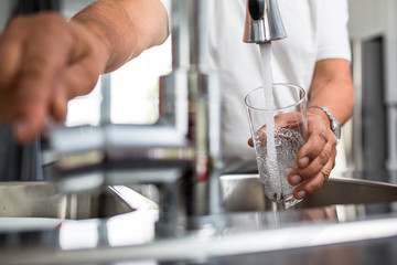 Hands of a senior man pouring a glass of water in a modern kitchen