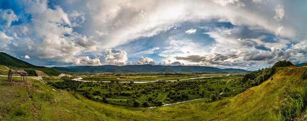 Panorama of lush green river valley at sunset with sun rays and dramatic sky. The area is known as Shangri-la. North Yunnan, China. © Niccolo