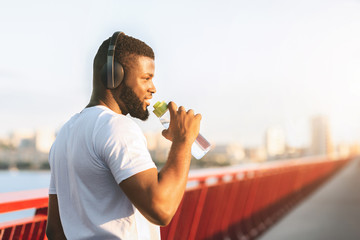 Young black man drinking water on the bridge