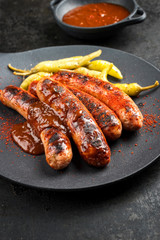 Traditional barbecue German Bratwurst with hot sauce and peperoni as closeup on a modern design cast iron plate