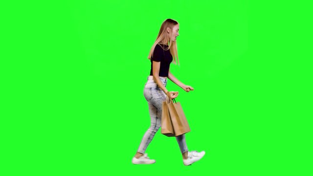 Excited shopper with shopping bags dances and walks cheerfully in full shot over green screen.