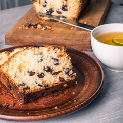 Sliced homemade raisin cake on a clay plate close-up and a cup of tea with lime.