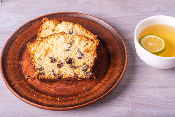Sliced homemade raisin cake on a clay plate close-up and a cup of tea with lime.
