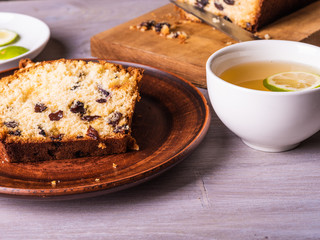 Sliced homemade raisin cake on a clay plate close-up and a cup of tea with lime.