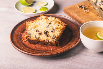 Sliced homemade raisin cake on a clay plate close-up and a cup of tea with lime.