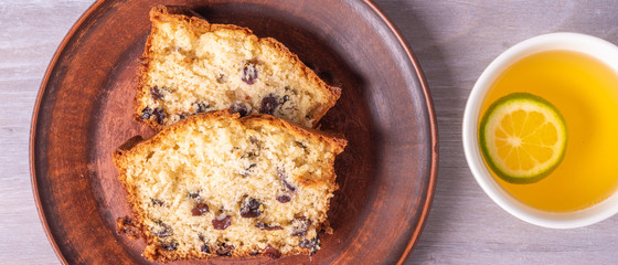 Sliced homemade raisin cupcake on a clay plate close-up and a cup of tea with lime. Top view