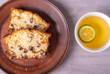 Sliced homemade raisin cupcake on a clay plate close-up and a cup of tea with lime. Top view