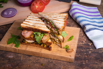 Delicious sandwich cut into triangles - toasted bread with chicken breast, fried bacon, vegetables, pickles with mustard and arugula close-up on a rustic table, top view