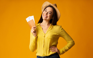 Happy tourist girl holding tickets and passport on yellow background