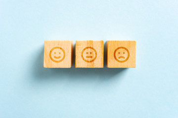 Happy, neutral and frown face on wood blocks toys and blue background. Rating concept.