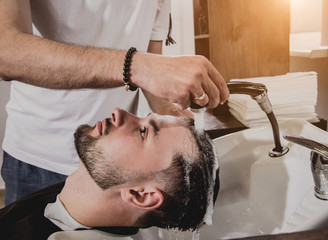 Young man with trendy haircut at barber shop. Barber washes customer head.