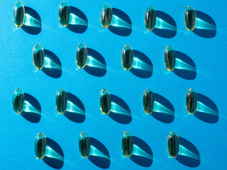 Top view of Omega 3 capsules pattern with a reflection on blue background