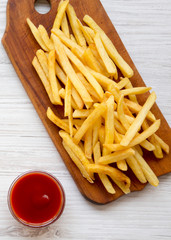 French fries on a rustic wooden board and ketchup on a white wooden surface, top view. From above, flat lay, overhead.