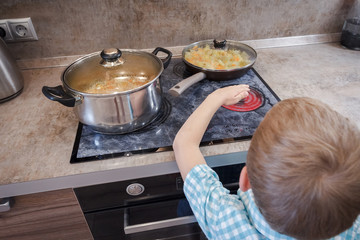 Kid risking accident with cooker in kitchen. Hazard at home. Concept of burn children