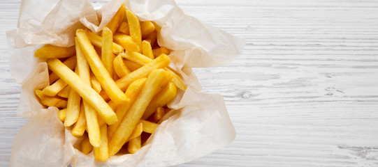 French fries in a paper box over white wooden background, top view. Flat lay, overhead, from above. Copy space.
