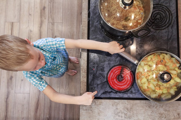 Little boy playing with pan and hot electric stove in the kitchen