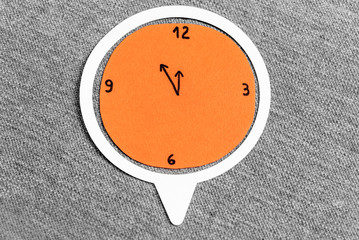 Time to lunch concept. Orange clock made with paper on a grey fabric textured background.