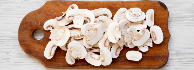 Chopped mushrooms on a rustic wooden chopping board on a white wooden background, top view....