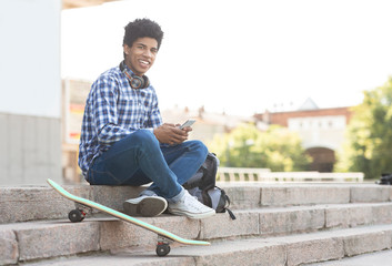 Obraz premium Cheerful teenager using smartphone sitting on stairs against cityscape